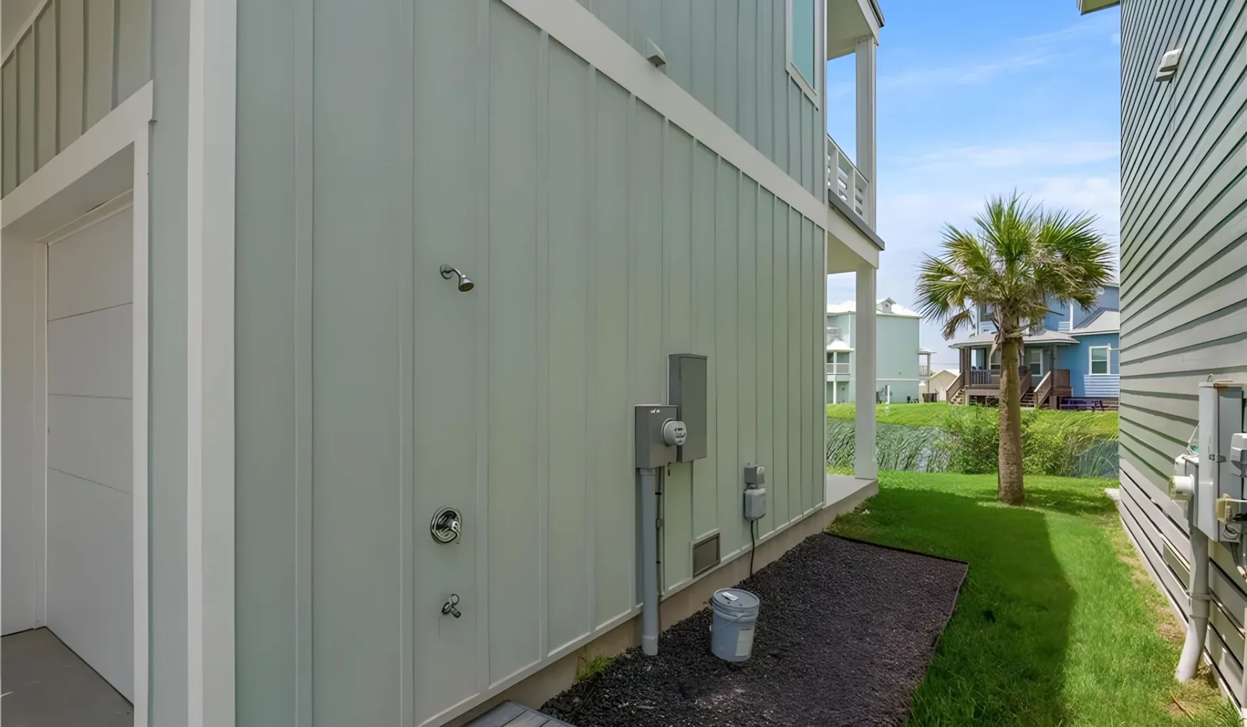 A narrow grassy passage runs between two buildings, with a palm tree beyond.