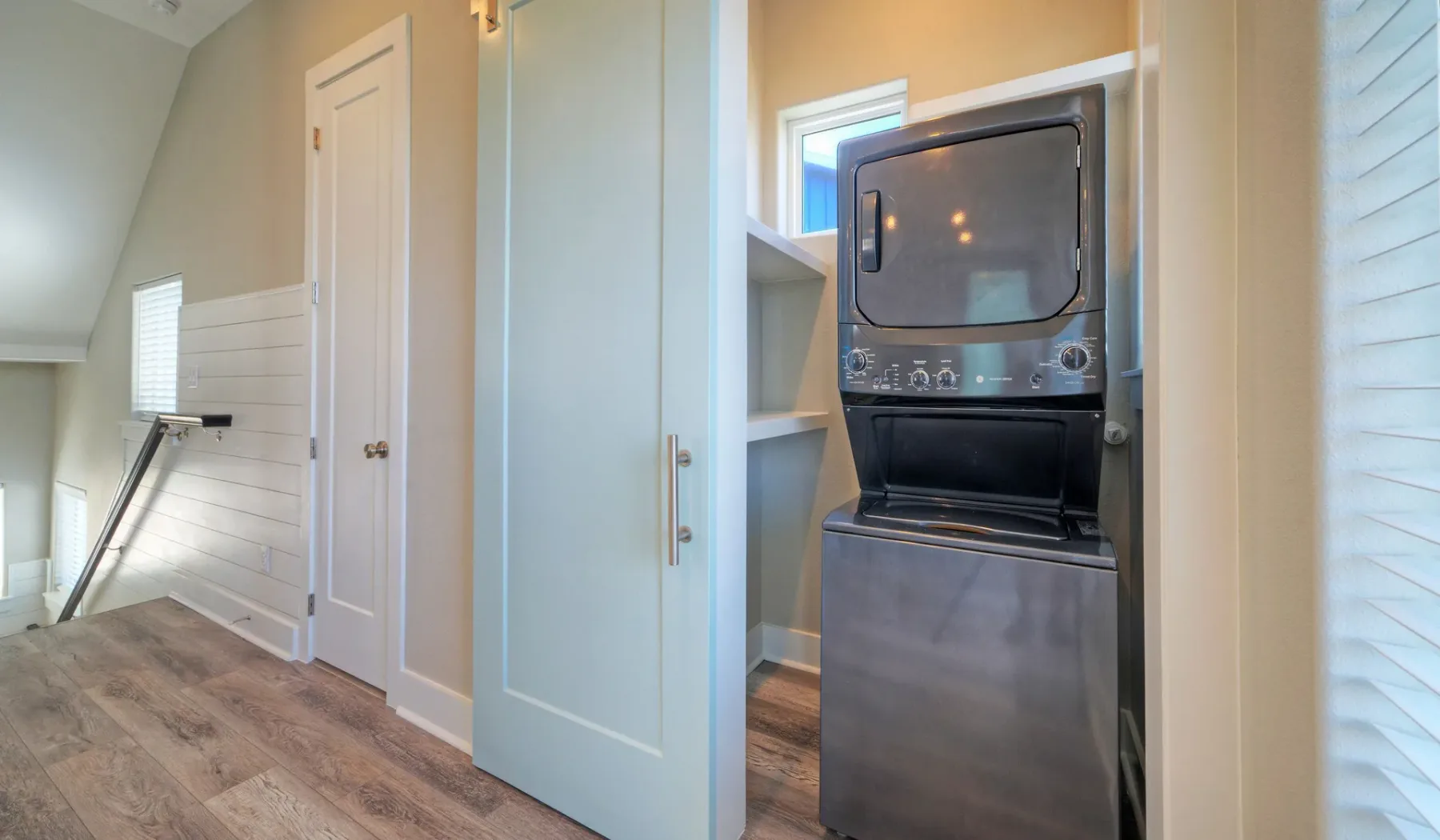 A laundry area with a stacked washer and dryer beside a pale blue door.