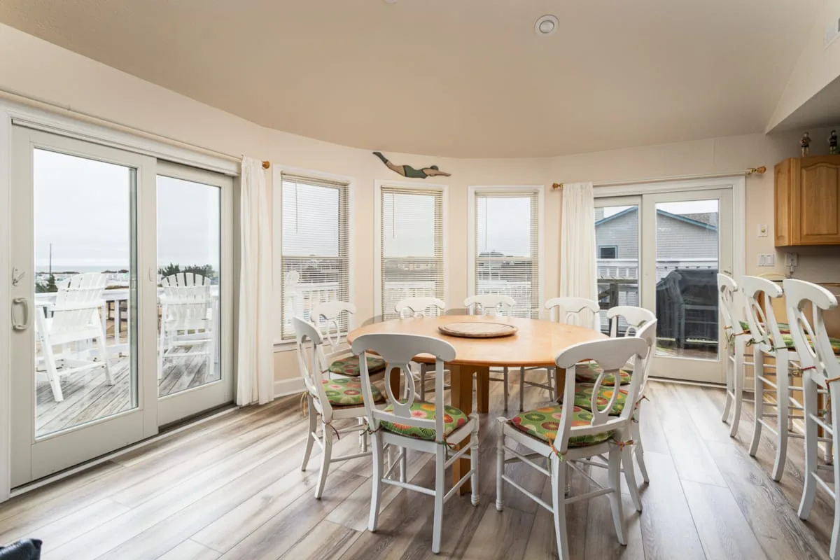 Un comedor luminoso con una mesa de madera y sillas junto a grandes ventanas.