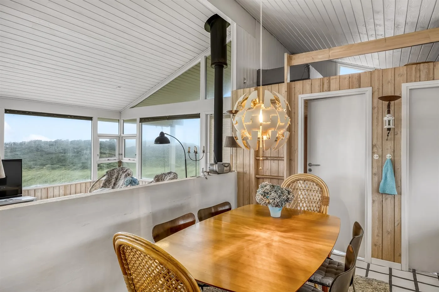 Comedor con una mesa de madera y grandes ventanales con vistas a zonas verdes.