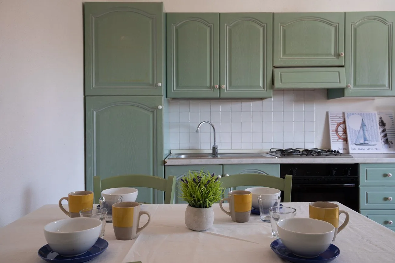 A kitchen with green cabinets, a tiled backsplash, and a set dining table.