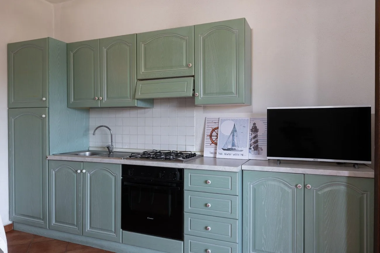 Una cocina con gabinetes verdes, una estufa y un televisor sobre la encimera.