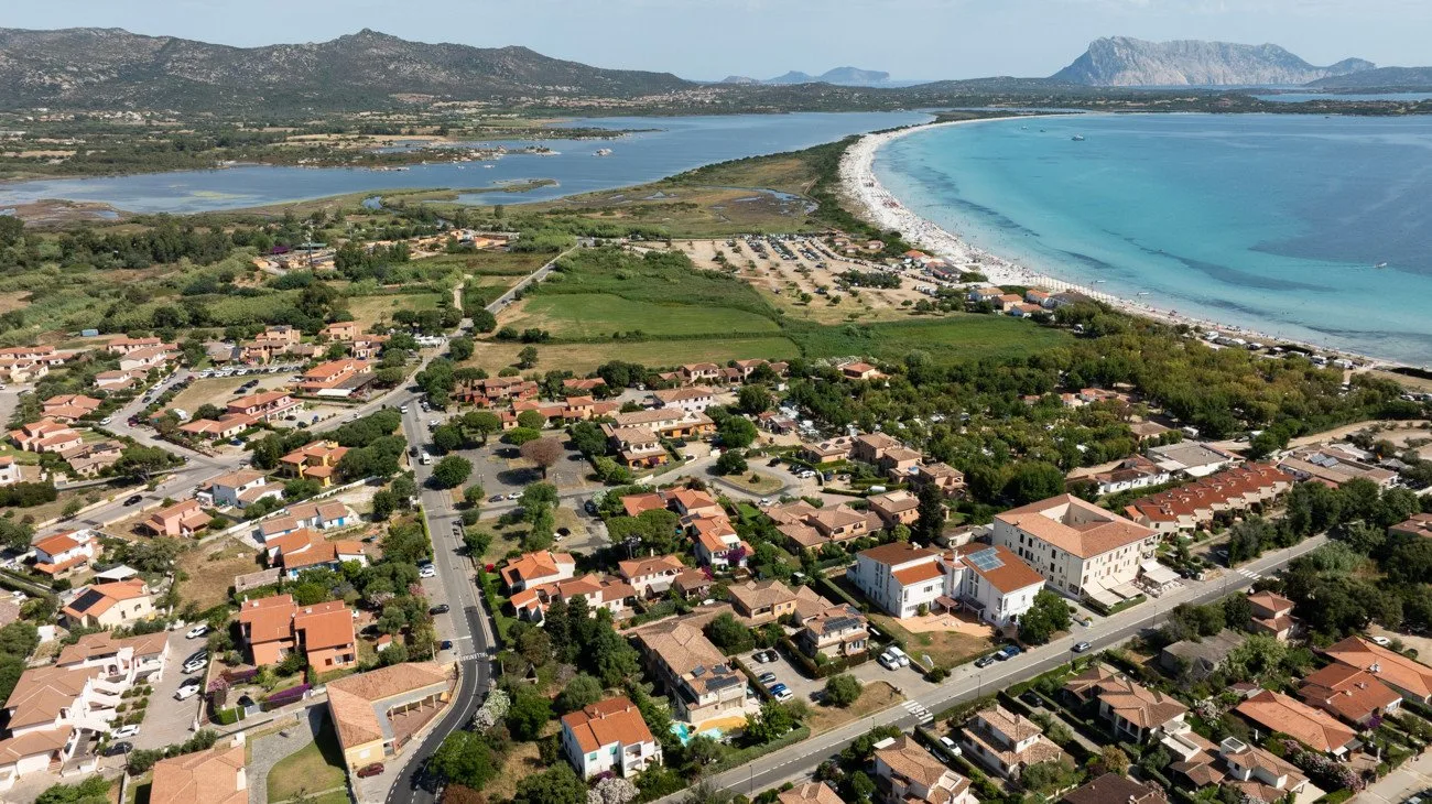 Aerial view of a coastal town beside a curving beach and turquoise water.