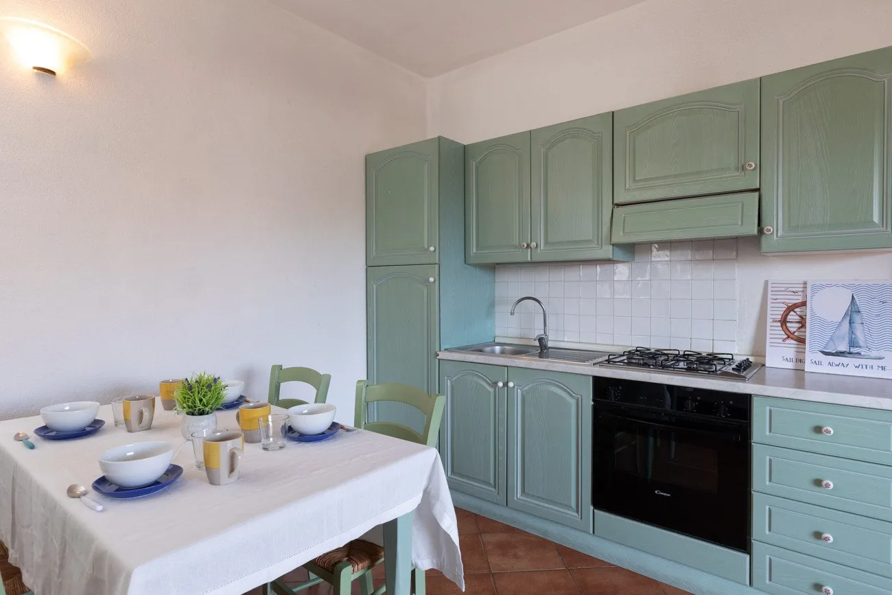 A kitchen with green cabinets, a stove, and a dining table set with dishes.