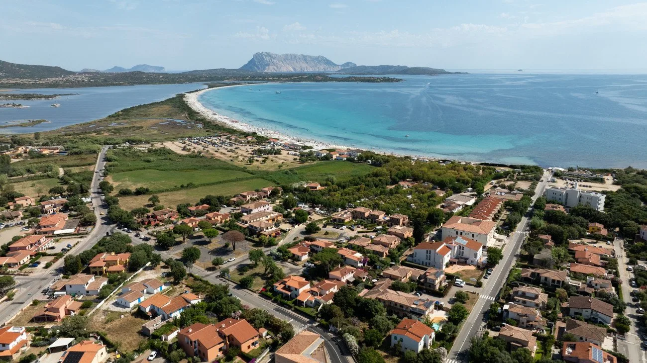 Aerial view of a coastal neighborhood beside a curved sandy beach and turquoise water.