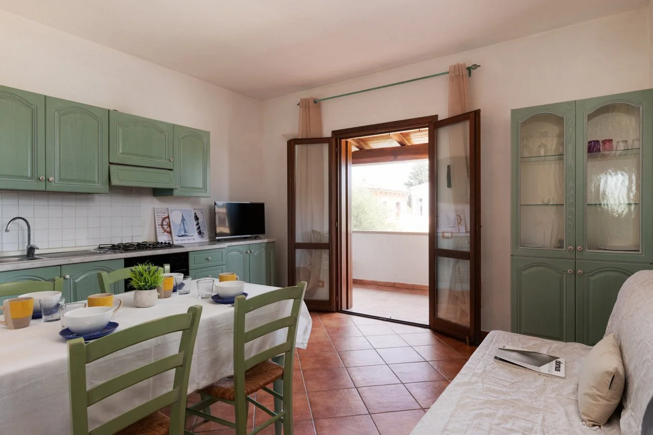 Comedor junto a una cocina compacta, con una puerta abierta que da al exterior.