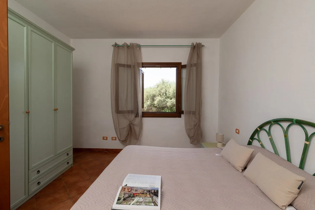 A bedroom with a bed, green wardrobe, and a window framed by sheer curtains.