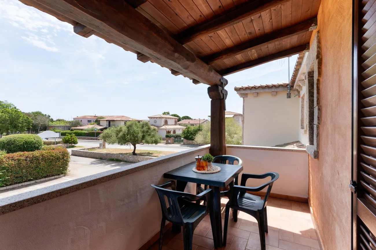 Una terraza cubierta con mesa y sillas tiene vistas a casas cercanas y vegetación.