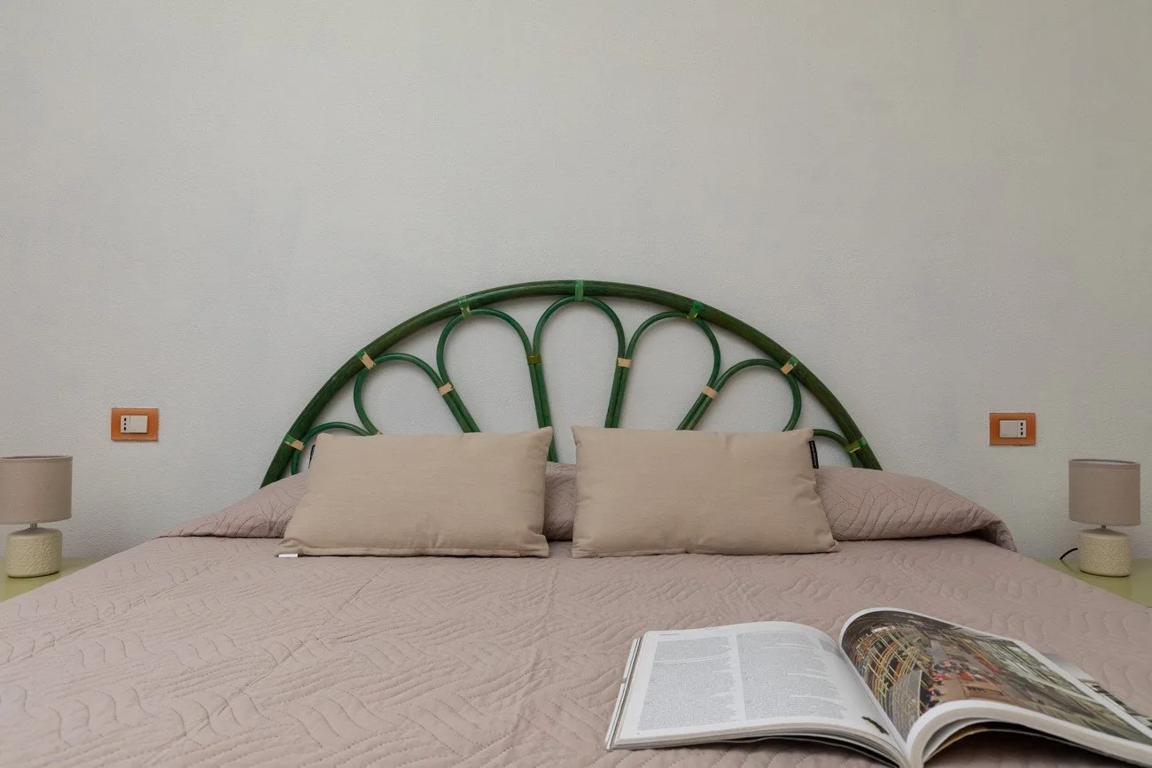 A bedroom with a bed, green arched headboard, and an open book.