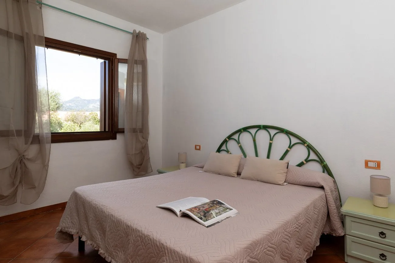 Un dormitorio con una cama junto a una ventana y una revista abierta.