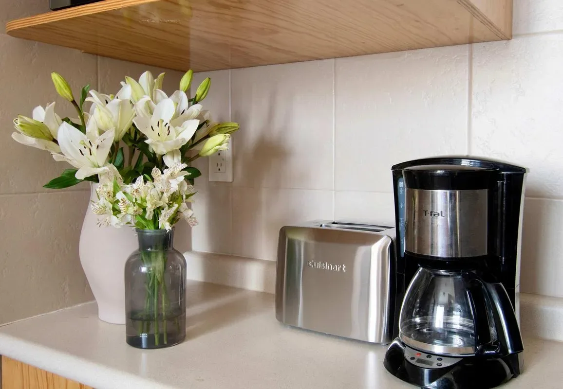 A kitchen counter holds a coffee maker, toaster, and vase of flowers.
