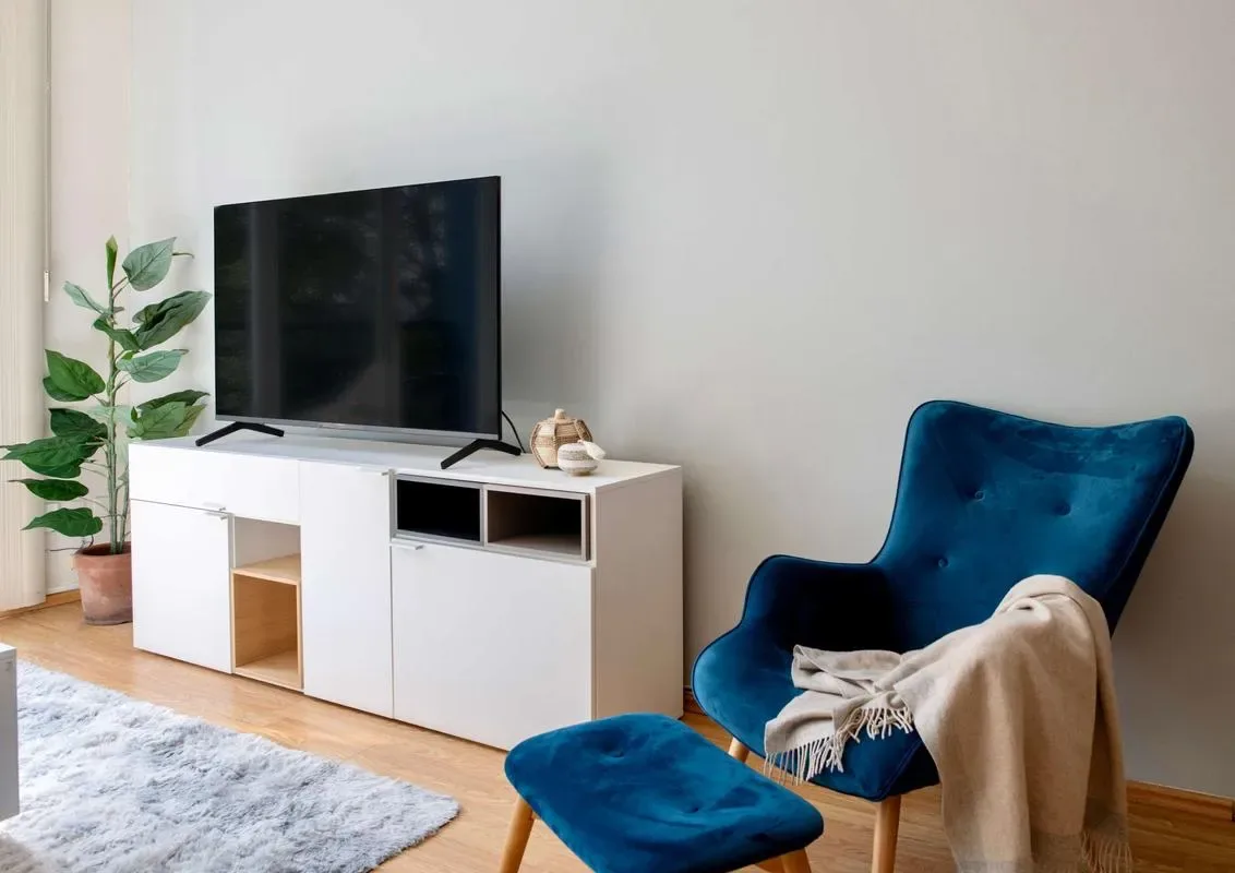 A living room with a television, blue seating, and a light-colored rug.