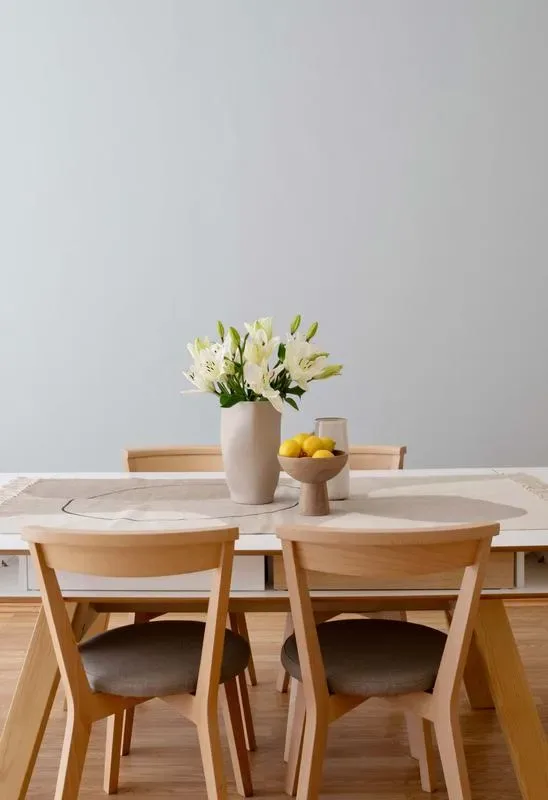 A wooden dining table is set with flowers and a bowl of lemons.