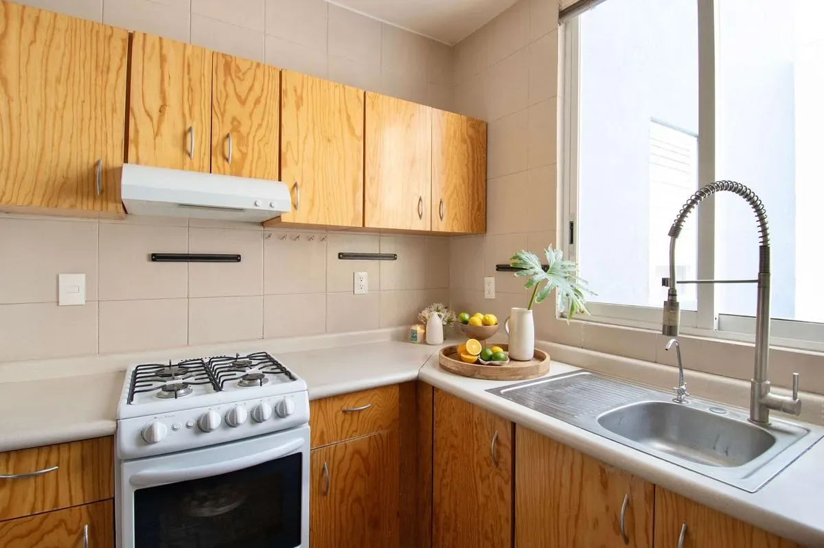 A kitchen with wooden cabinets, a stove, and a sink beside a window.