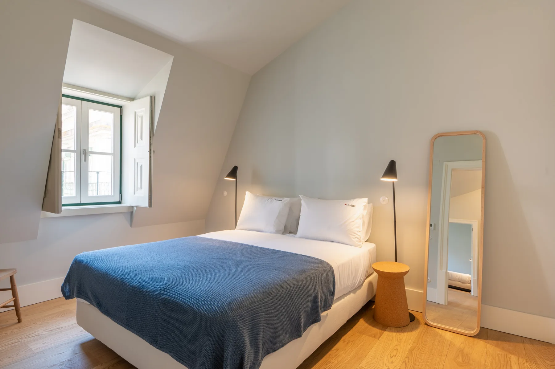 Un dormitorio luminoso con una cama vestida de azul y una ventana.