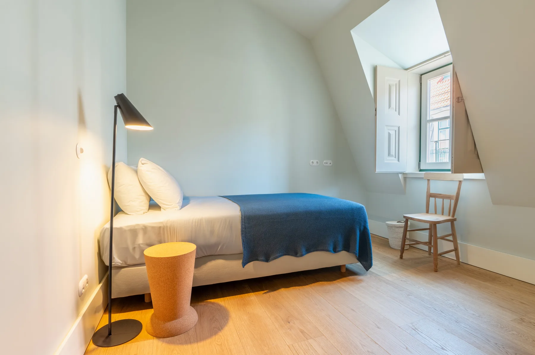 Un dormitorio luminoso con una cama y una ventana abierta.