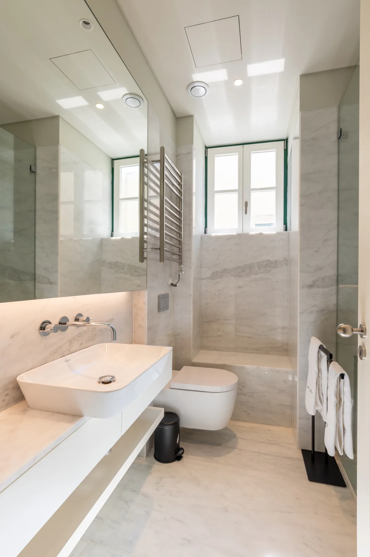 Un baño luminoso con lavabo de pared y una ventana.