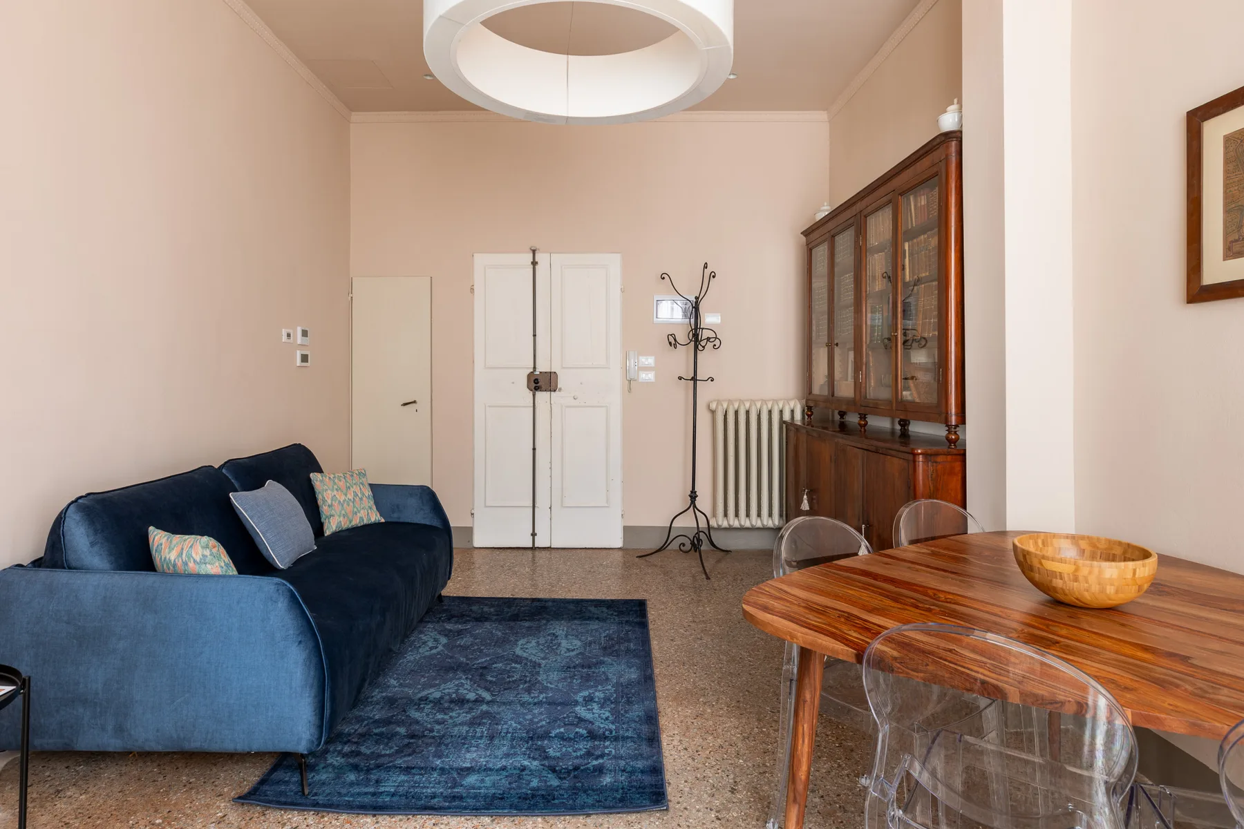 Una sala de estar con asientos azules, una mesa de comedor de madera y un gabinete con puertas de vidrio.