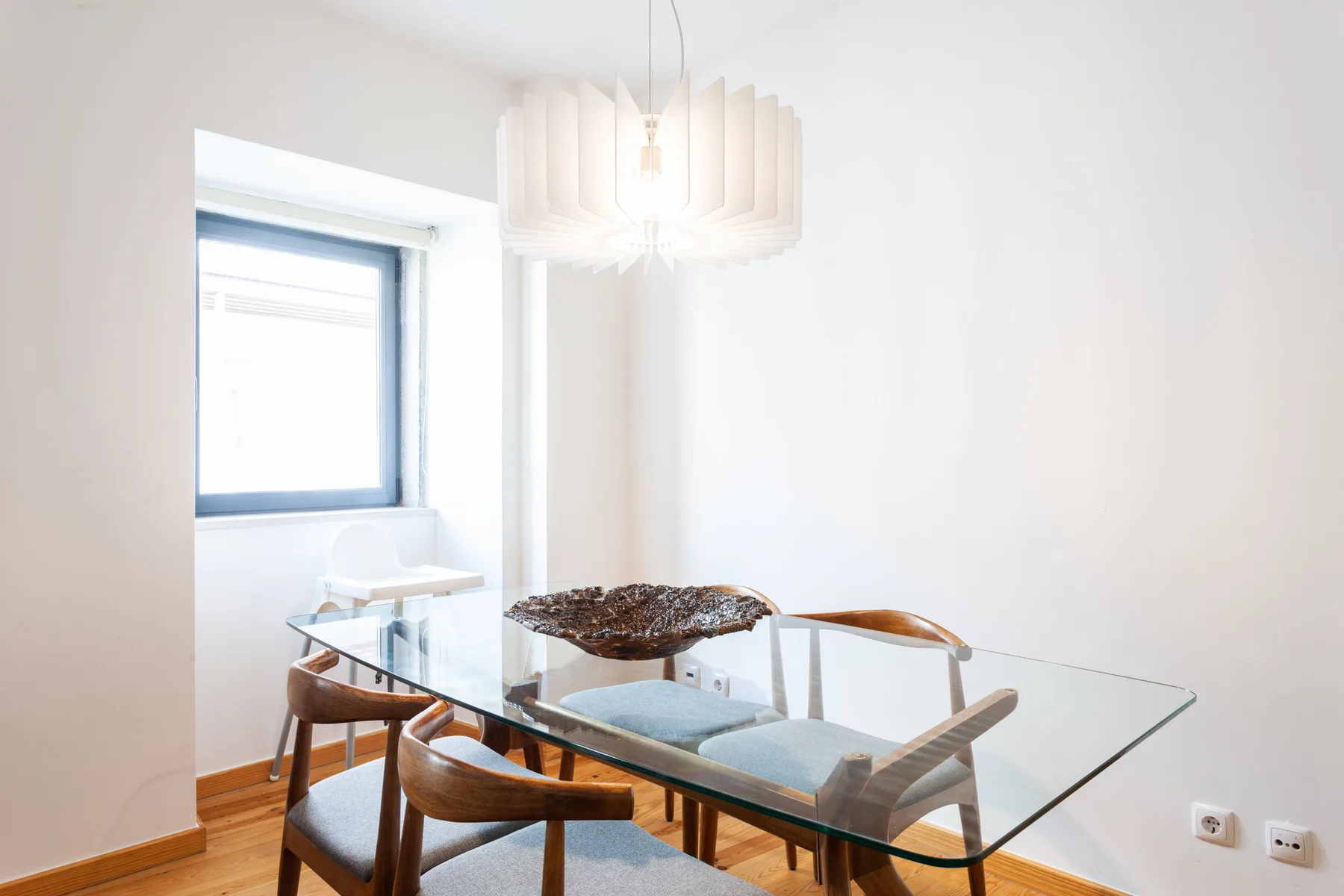 A bright dining area with a glass table and chairs beneath a hanging light.