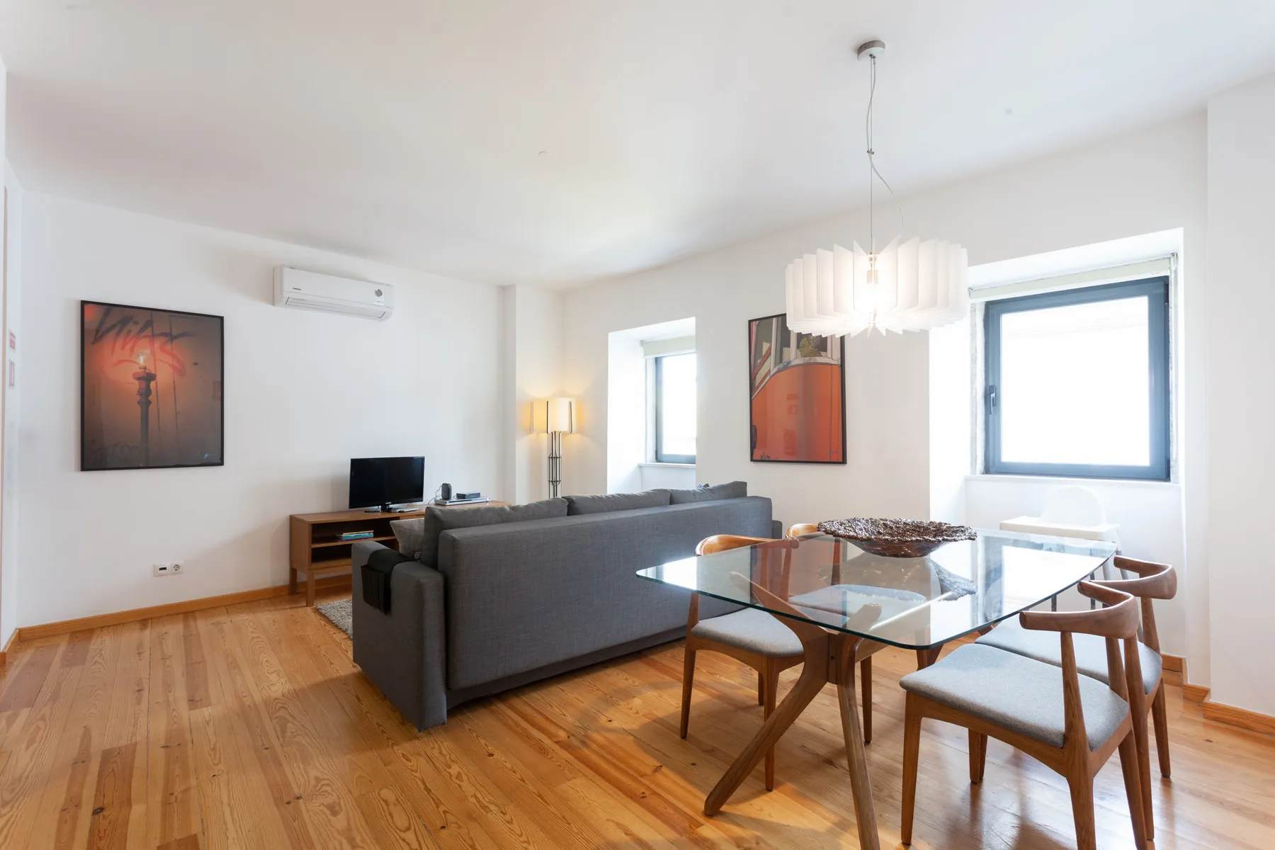 Una luminosa sala de estar y comedor con asientos grises y una mesa de cristal.