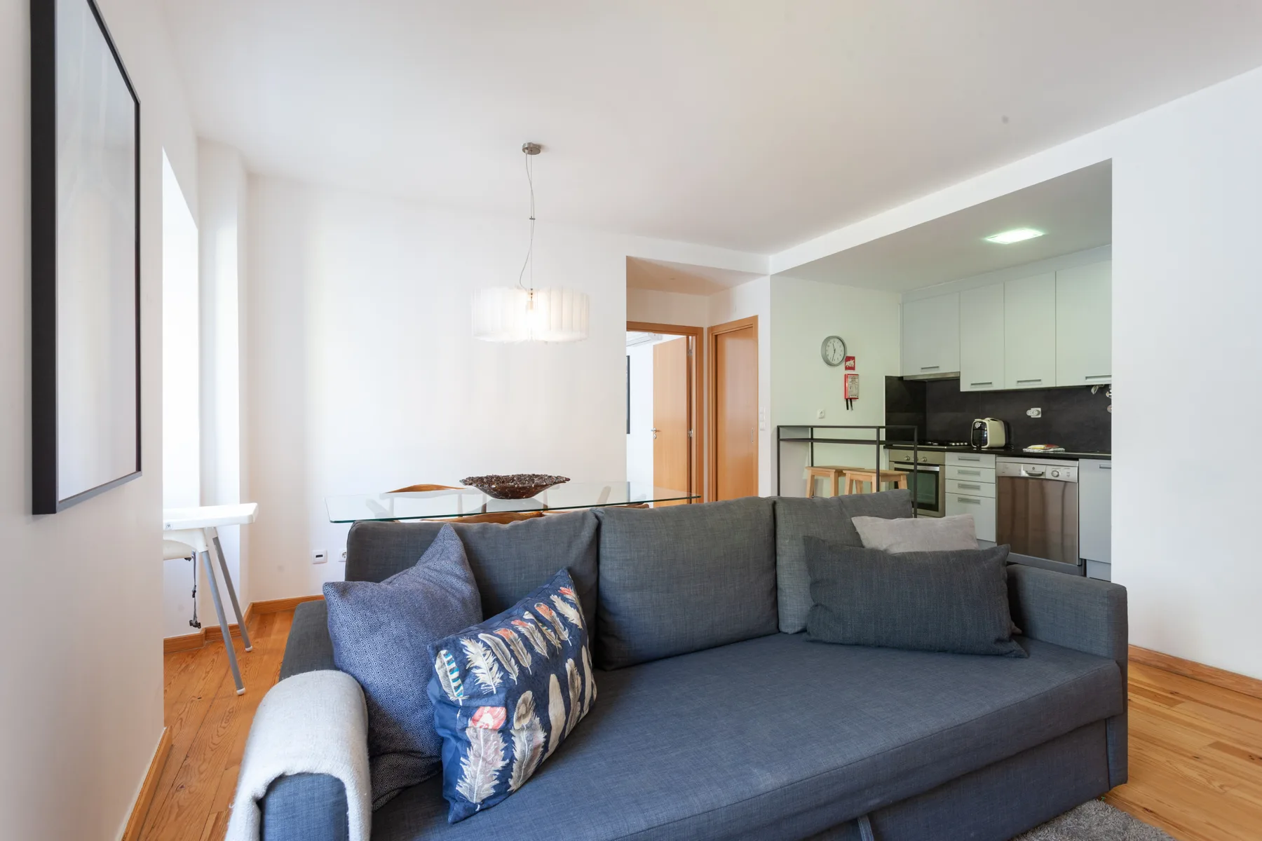 A living room with gray seating and an open kitchen behind it.