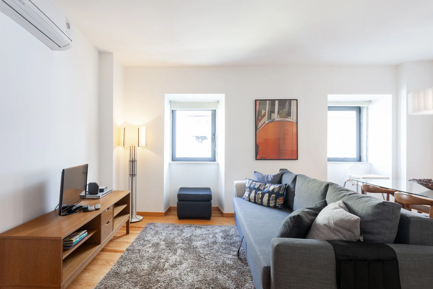 A bright living room with a gray seating area, rug, and two windows.