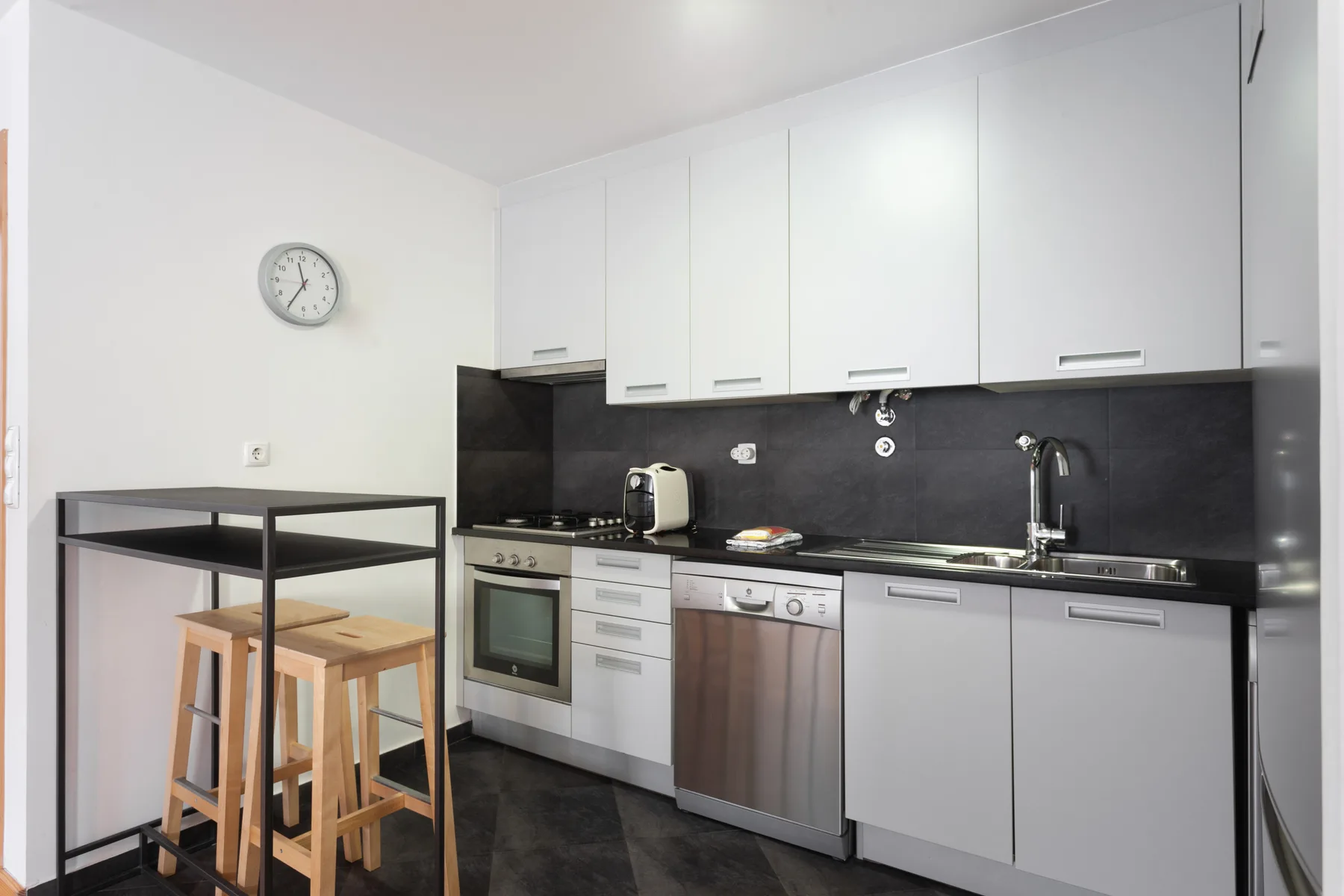 Una cocina moderna con armarios blancos, encimeras oscuras y una pequeña mesa de comedor.
