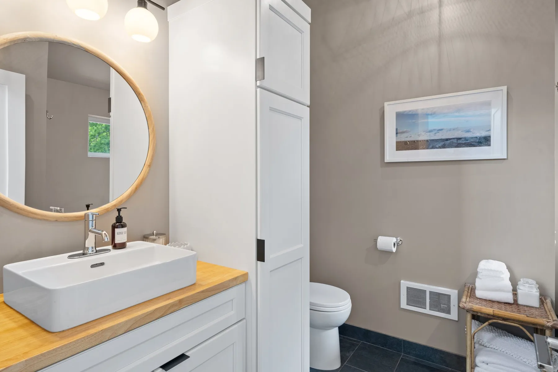 Un baño con lavabo, espejo redondo, inodoro y un cuadro enmarcado.