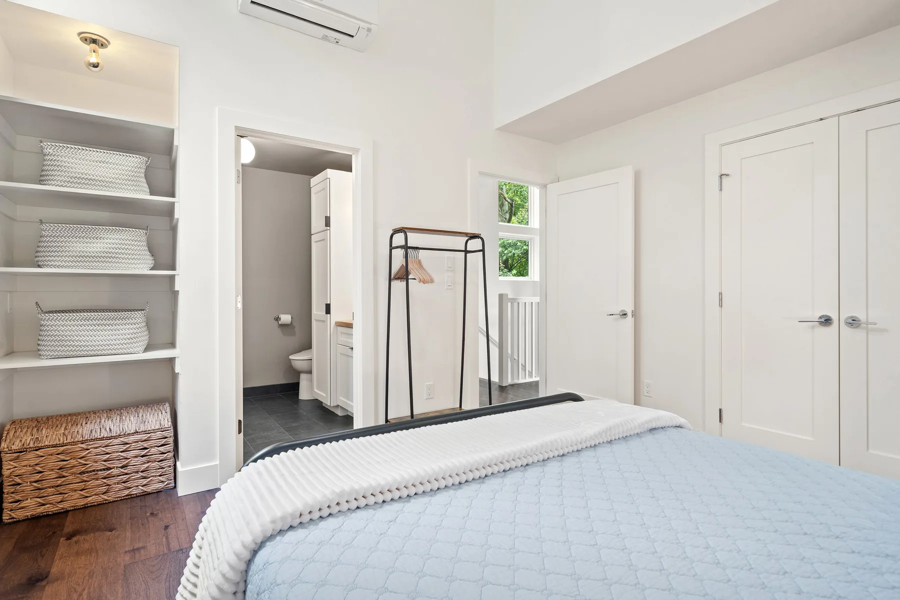 Un dormitorio luminoso con una cama, estantes empotrados y una puerta abierta.
