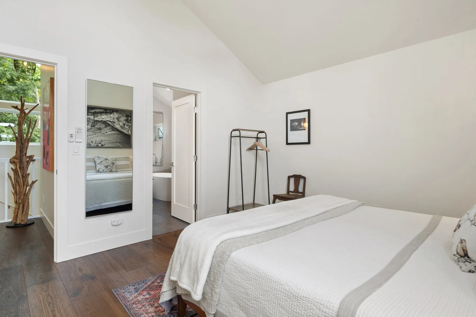 Un dormitorio luminoso con una cama bien tendida y un perchero.
