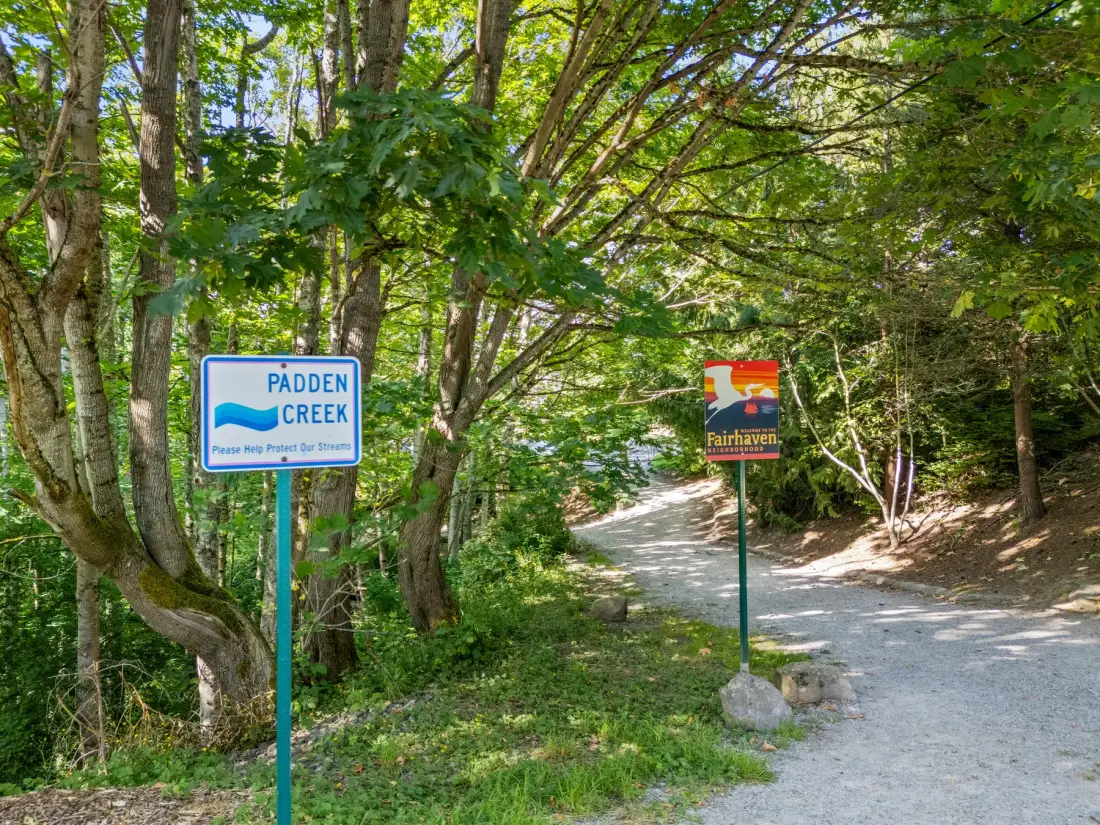 Un sendero de grava arbolado pasa junto a letreros de Padden Creek y Fairhaven.