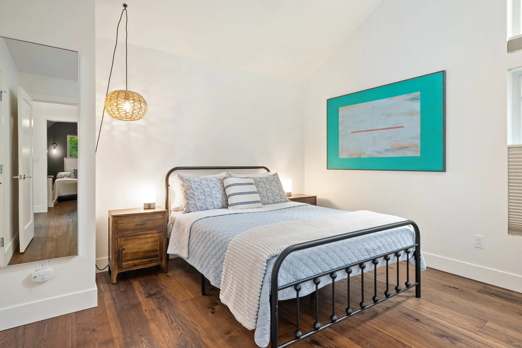 Un dormitorio luminoso con una cama, una mesita de madera y un cuadro en la pared.