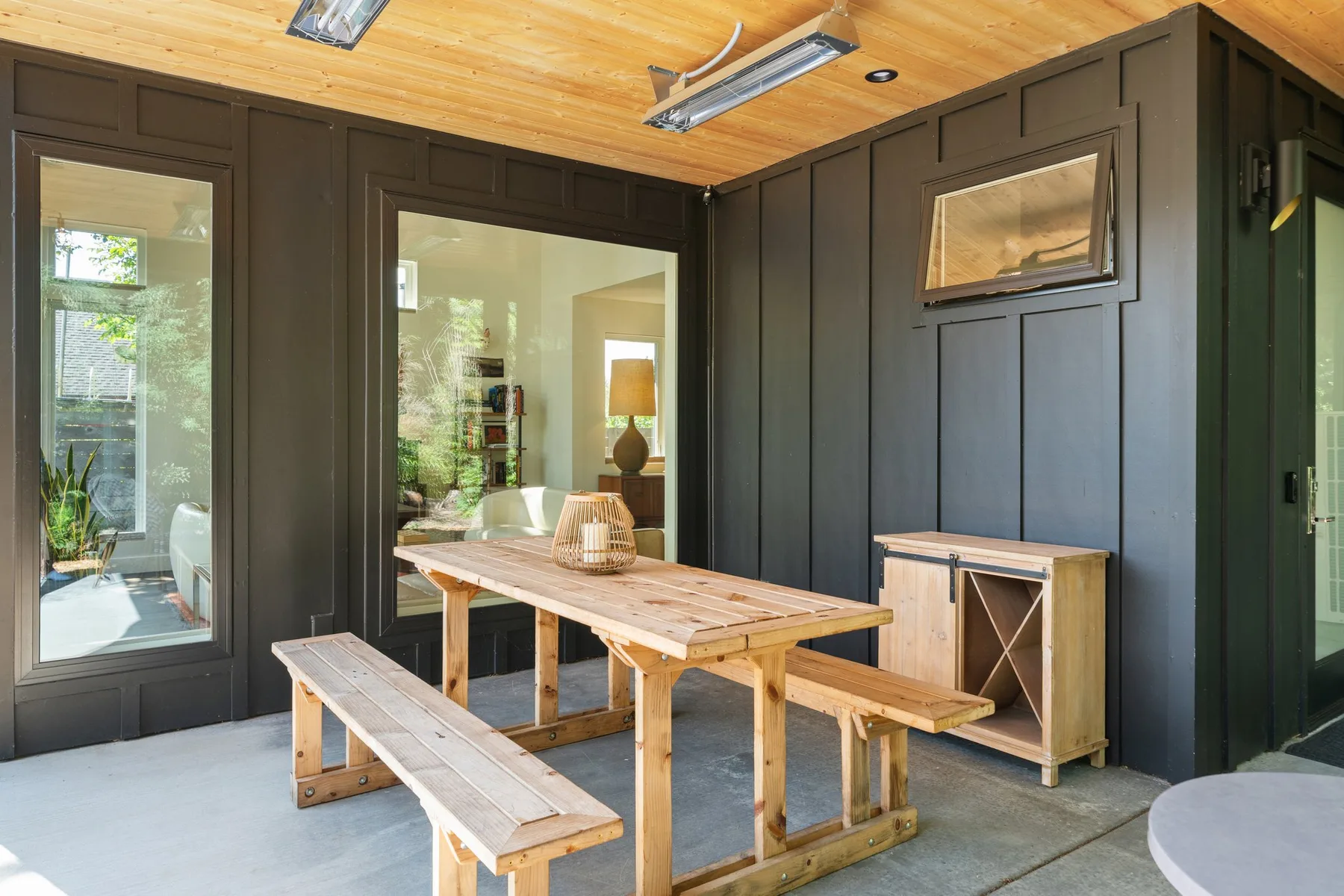 Comedor con una mesa de madera y bancos junto a grandes ventanas.