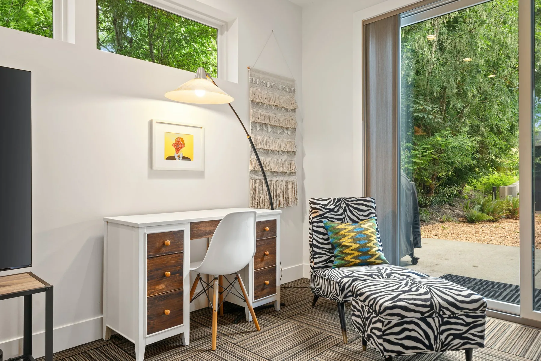 Una luminosa zona de estar tiene un escritorio, un sillón estampado y vistas al jardín.