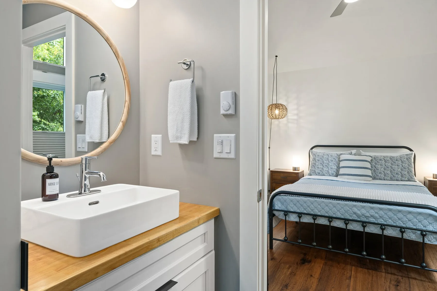 Dormitorio con una cama bien tendida junto a un tocador de baño y un espejo redondo.