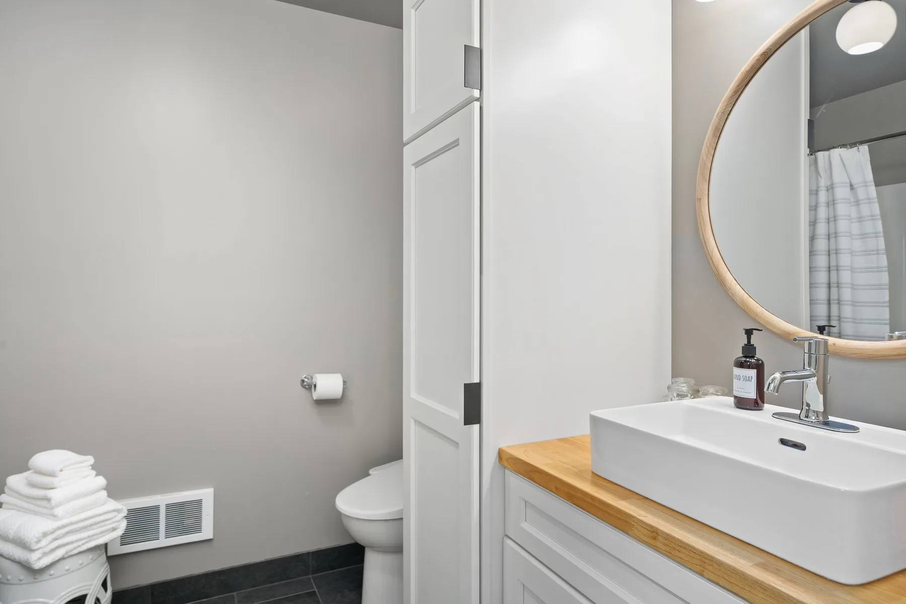 Un tocador de baño con lavabo y espejo redondo junto a un inodoro.