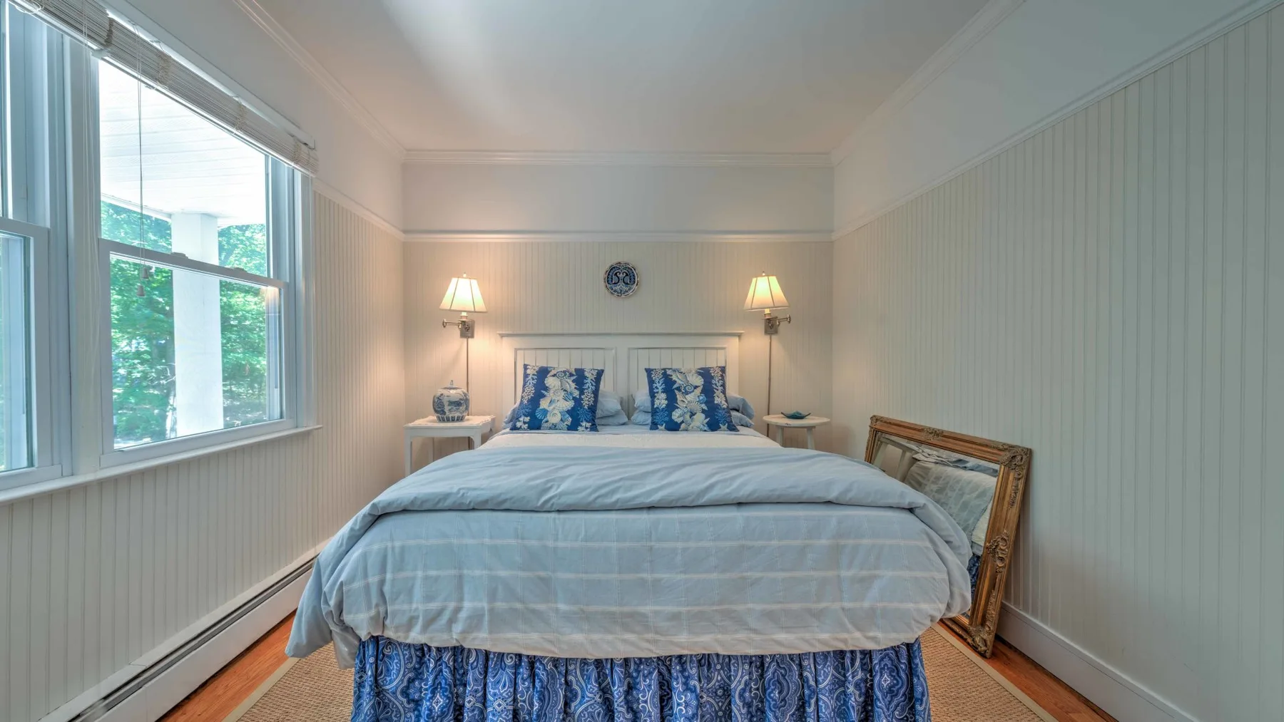 Dormitorio con una cama entre dos lámparas y una ventana amplia.