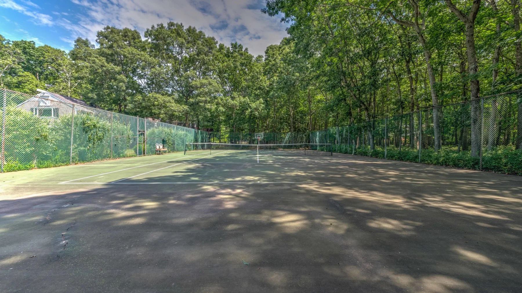 Una pista de tenis al aire libre está rodeada de árboles y una cerca.