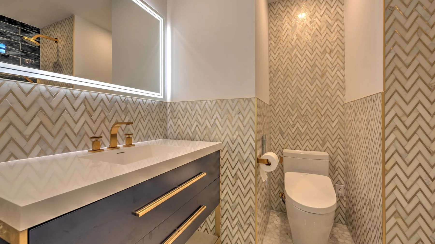 Un baño con un inodoro junto a un lavabo bajo un espejo iluminado.