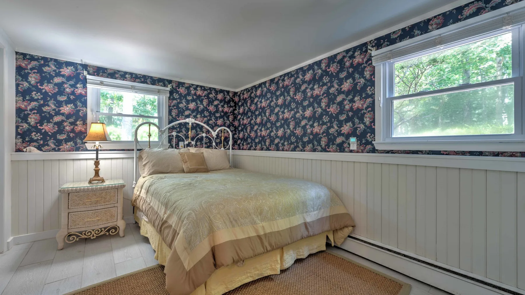 Un dormitorio con una cama, una mesita de noche y paredes con estampado floral.