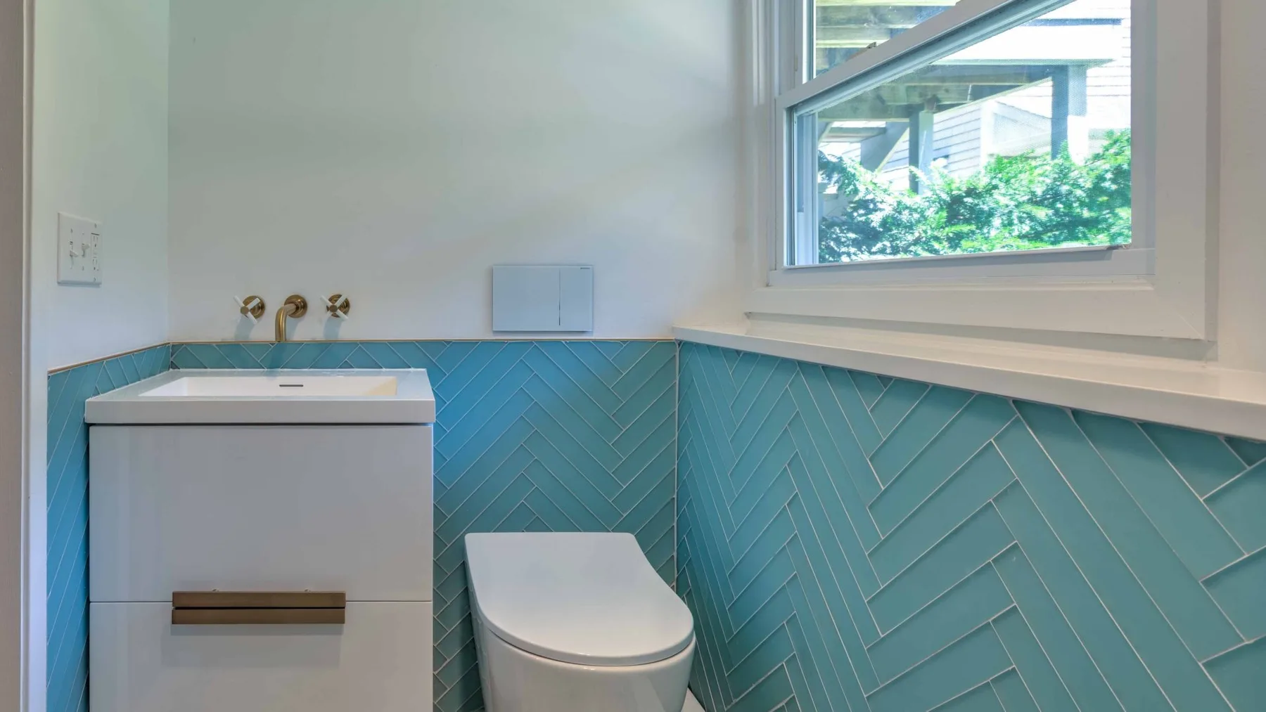Un baño con inodoro, paredes de azulejos y una ventana con vista a la vegetación.