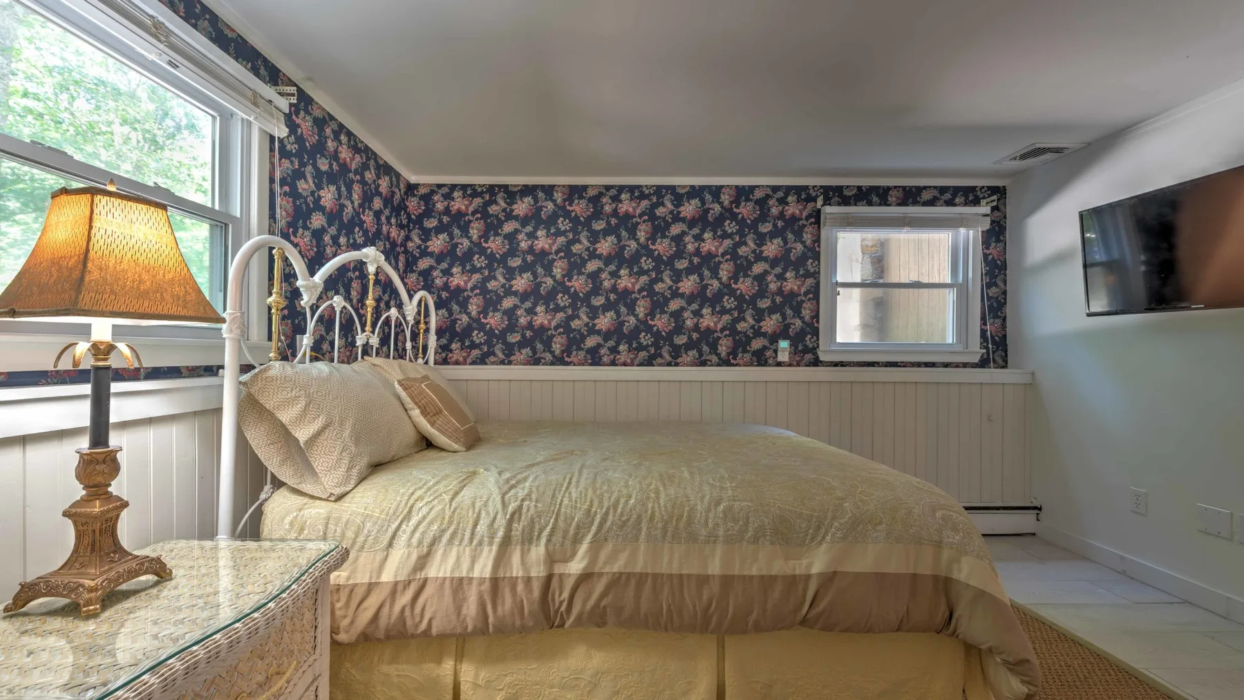 Un dormitorio con una cama bajo un papel tapiz floral y una ventana.
