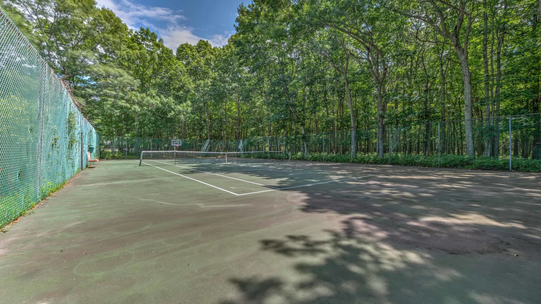 Una pista de tenis al aire libre está rodeada de árboles y cercas de malla.
