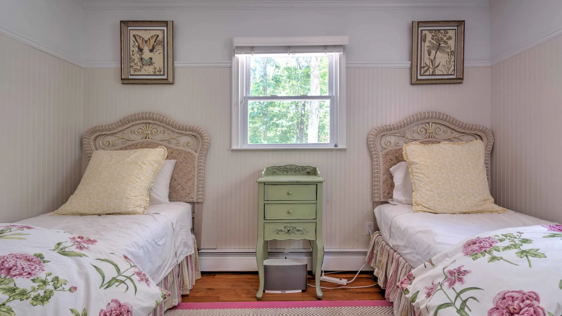Un dormitorio con dos camas y una mesita verde bajo la ventana.