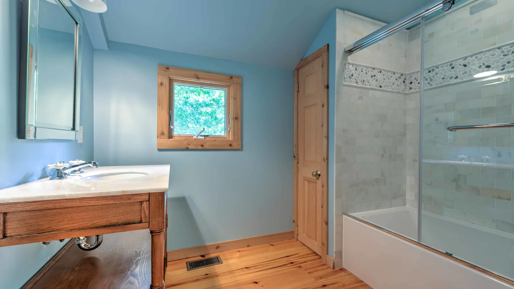 Un baño con un mueble de madera, una ventana y una bañera con ducha.