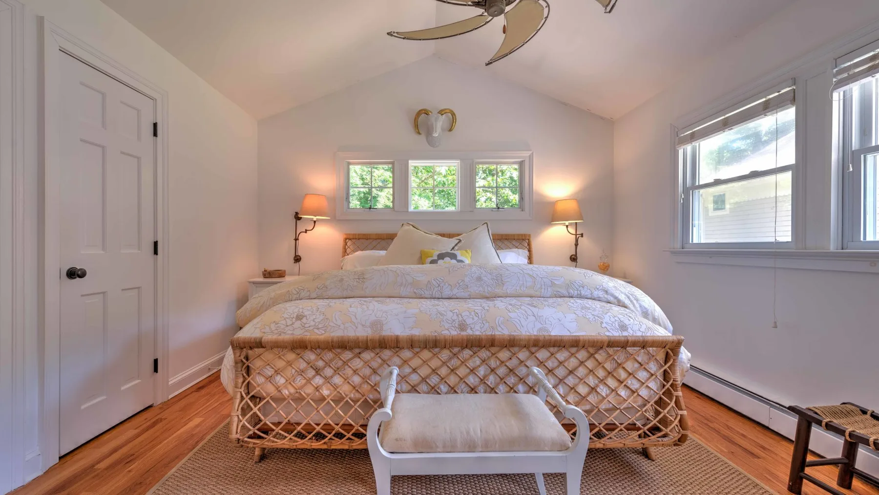Un dormitorio luminoso con una cama, lámparas de noche y ventanas grandes.