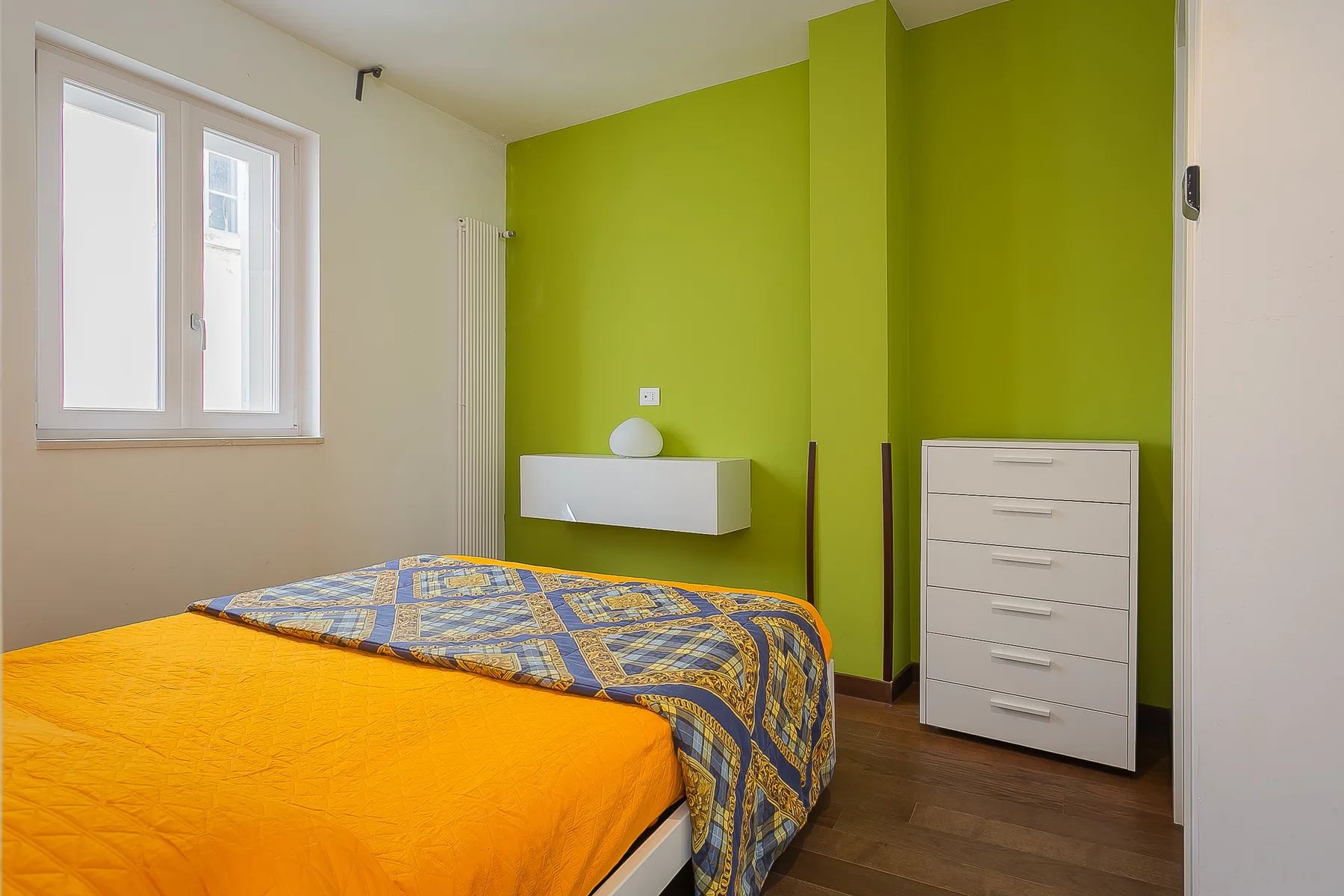 Un dormitorio con una cama junto a una pared verde brillante y una cómoda.