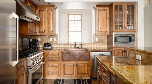 Una cocina con gabinetes de madera, un fregadero central y encimeras de piedra.