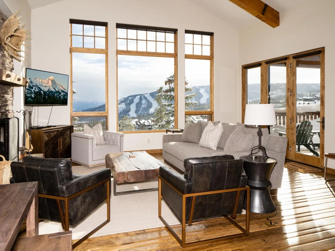 Una sala de estar con asientos alrededor de una mesa de centro junto a grandes ventanas.