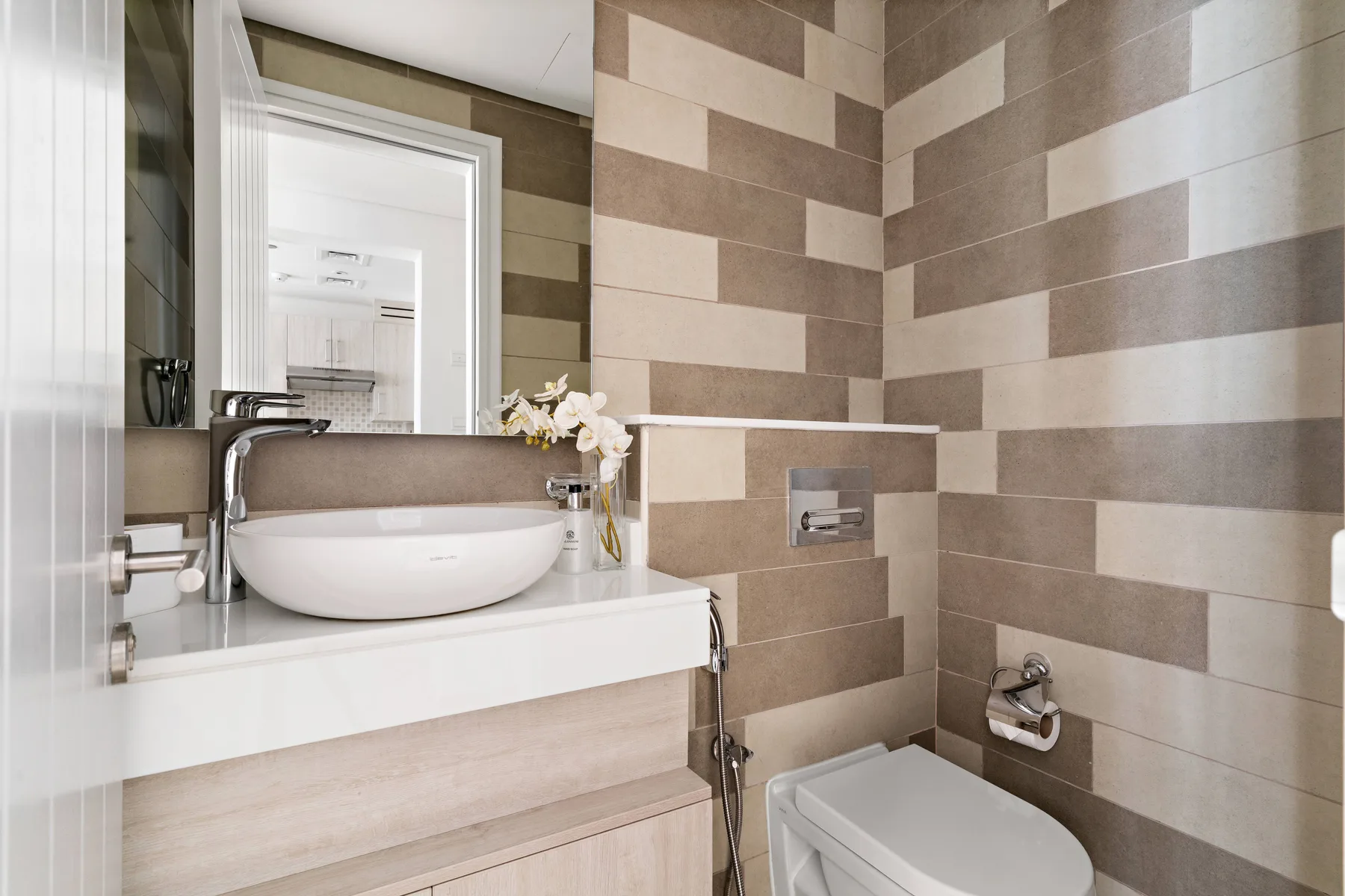 Un baño alicatado con lavabo sobre encimera, grifo de pared e inodoro.